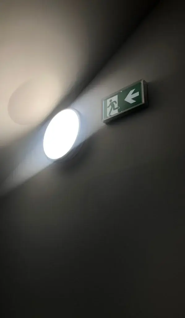 Lit emergency light beside an exit sign, powered from the area lighting circuit