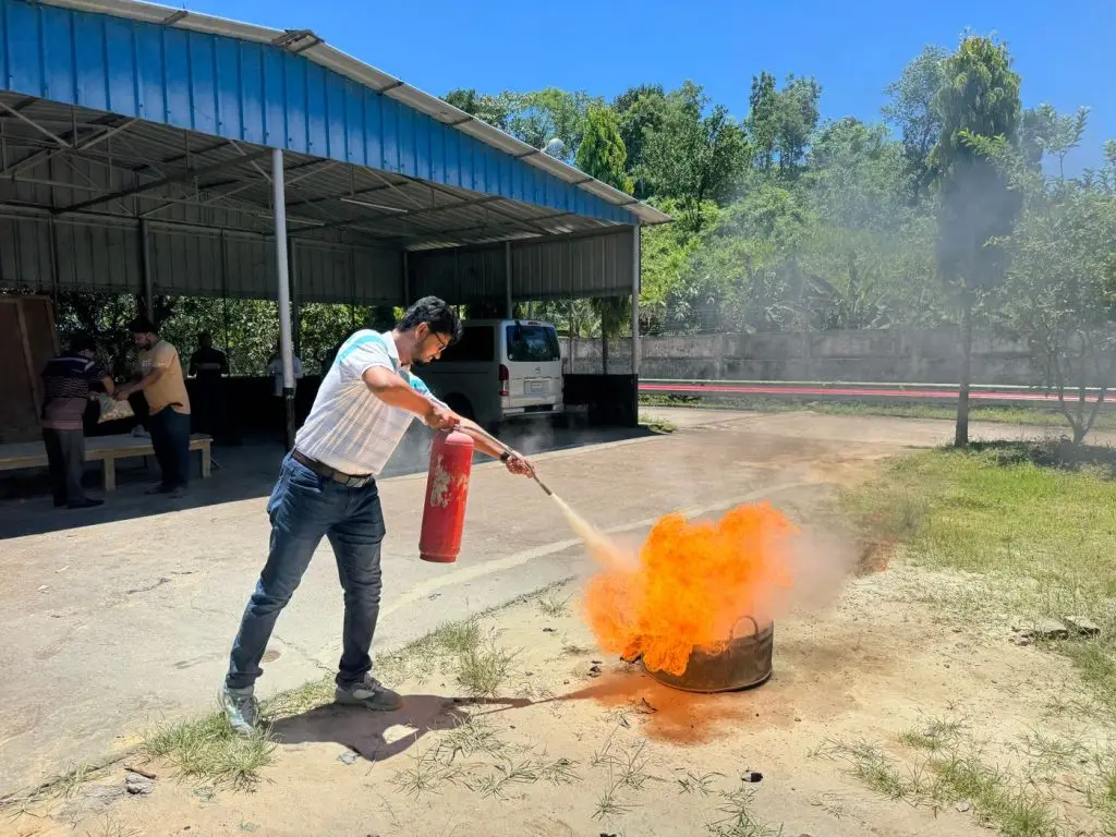 Person using a fire extinguisher on a small fire during fire safety training