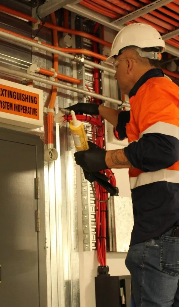 Technician applying fire-rated sealant to a service penetration as part of passive fire protection